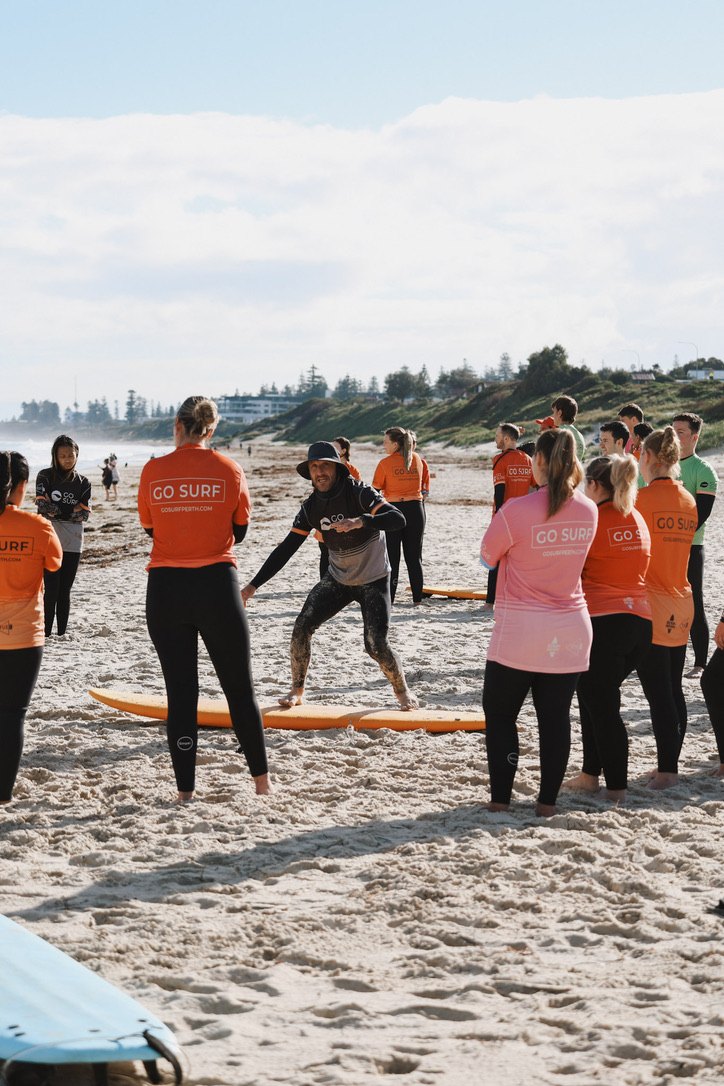 Go Surf coach showing newbies how to pop up on the sand
