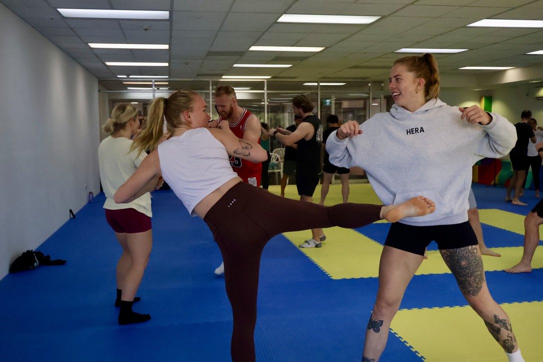 Two newbies laughing while practising kicks at a kickboxing social
