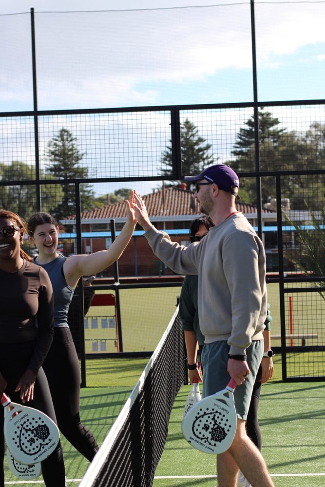 Newbies high-fiving over the net at a padel social